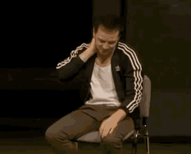 a man wearing an adidas jacket is sitting in a chair on a stage .