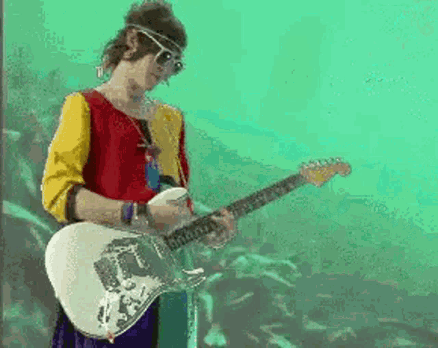 a man wearing sunglasses is playing a guitar in front of a fish tank .