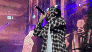 a man in a plaid shirt is singing into a microphone on stage