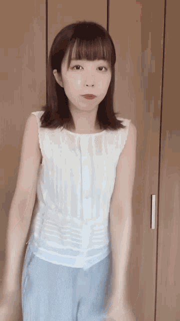 a young woman wearing a white tank top and blue pants is standing in front of a wooden wall .