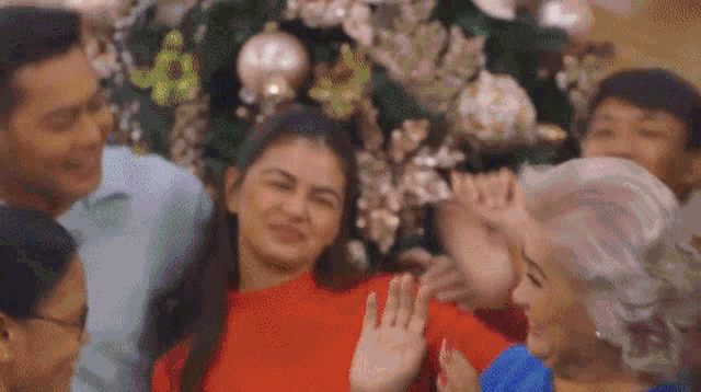 a woman in a red sweater is standing in front of a christmas tree with a group of people .