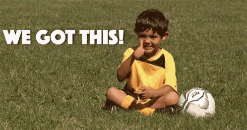 a young boy giving a thumbs up while sitting next to a soccer ball