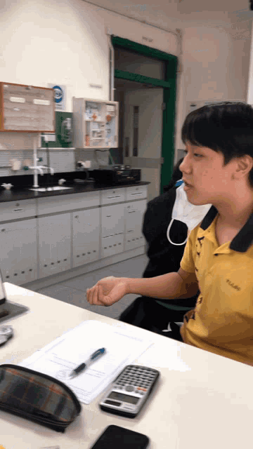 a man in a yellow columbia shirt sits at a desk with a calculator