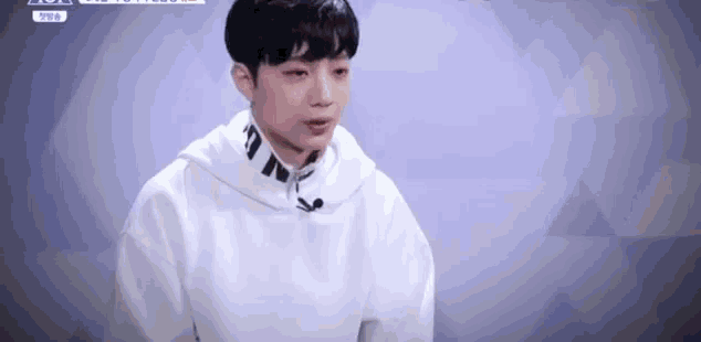 a young man in a white hoodie is sitting in front of a microphone on a stage .
