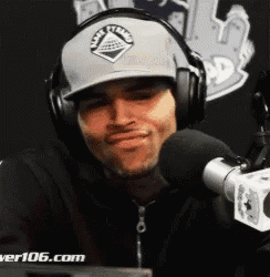 a man wearing headphones and a hat is standing in front of a microphone ..