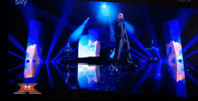 a man singing on a stage with a sky logo in the corner