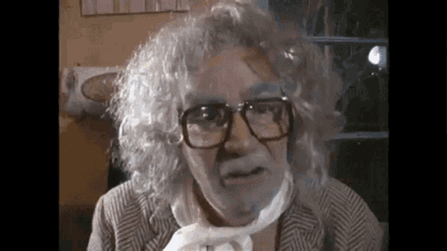a man with glasses and white paint on his face is wearing a suit .