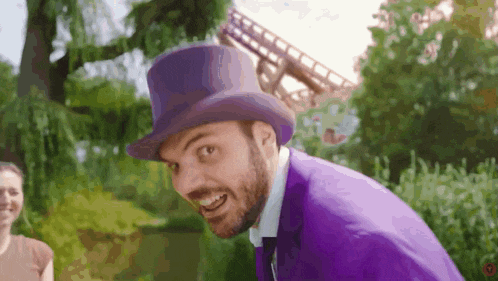a man in a purple suit and top hat smiles