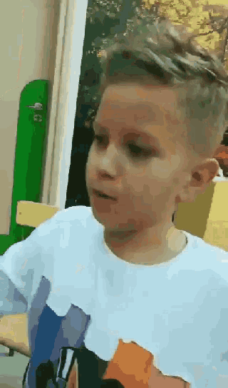 a young boy in a white t-shirt looks at something