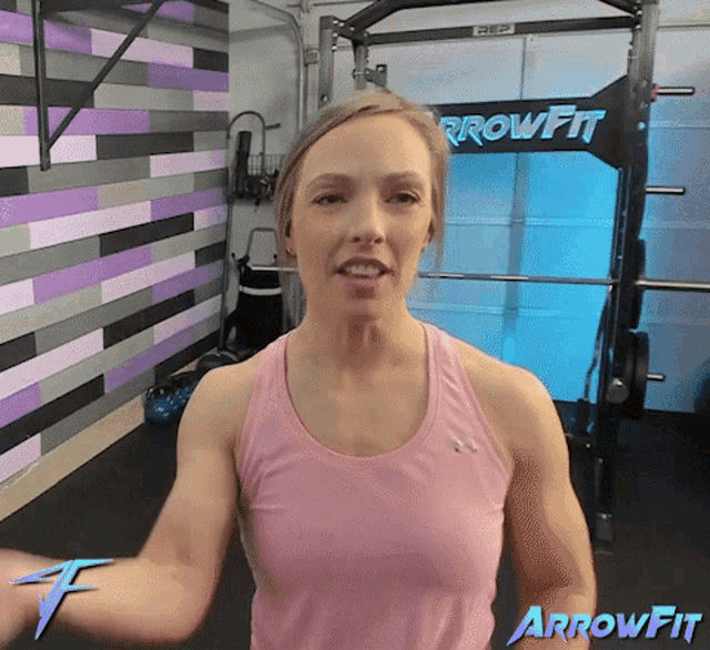 a woman in a pink tank top is standing in front of an arrowfit sign