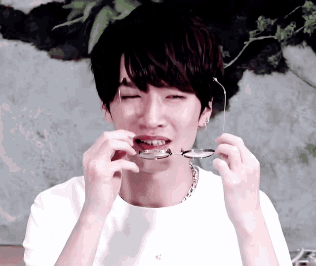 a young man wearing a white t-shirt is holding a pair of glasses in his mouth