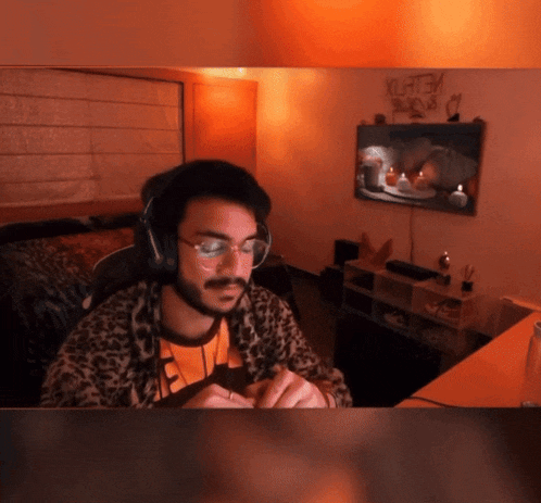 a man wearing headphones and glasses sits in front of a tv with a sign on the wall that says yurtgm