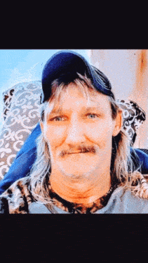 a man with long hair and a mustache is sitting in a chair .