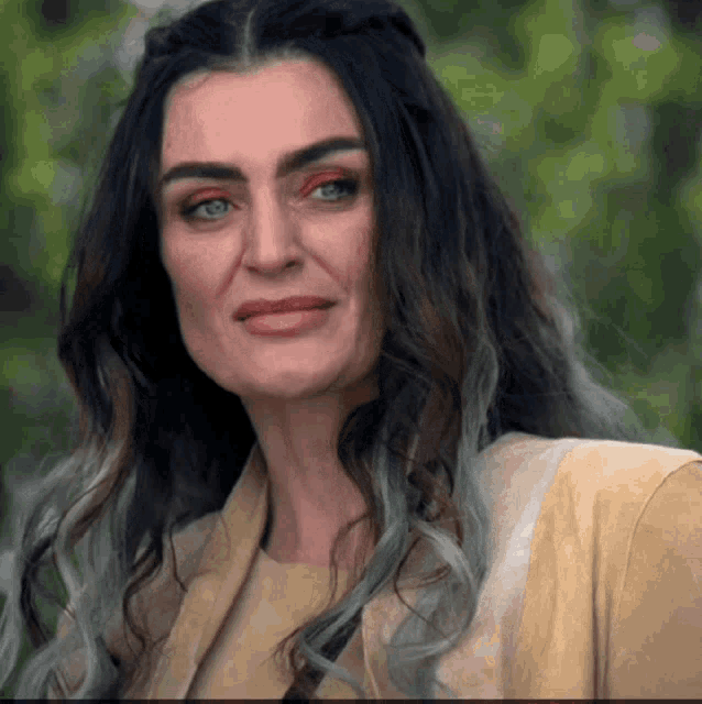 a woman with long dark hair is wearing a tan jacket and making a funny face