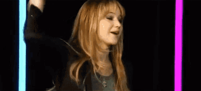 a woman with long blonde hair and bangs is standing in front of a pink light .