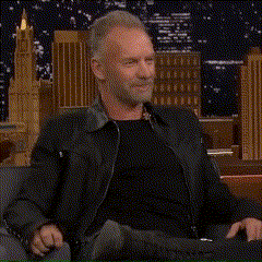 a man in a black jacket is sitting on a couch making a funny face