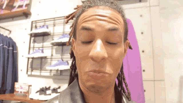 a man with dreadlocks is making a funny face in front of a rack of shoes