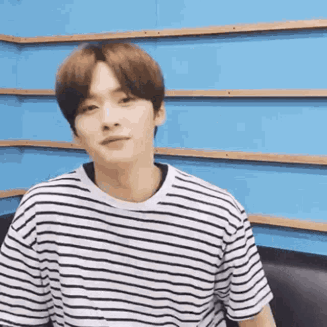 a young man wearing a striped t-shirt is sitting on a couch in front of a blue wall .