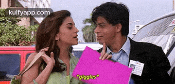 a man and a woman are standing next to each other and the woman is holding a pink piece of paper that says giggles