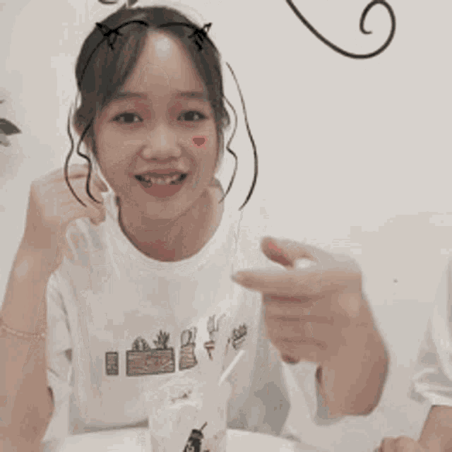 a girl wearing a cat ear headband is sitting at a table with a cup of ice cream