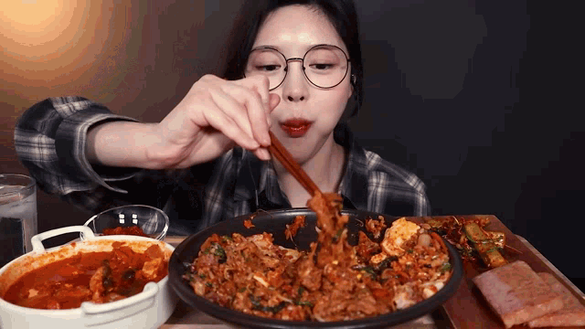 a woman wearing glasses is eating a large plate of food with chopsticks
