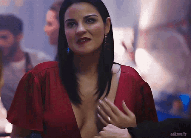 a woman in a red dress with a plunging neckline is being touched by a man 's hand .