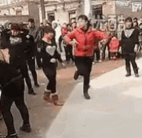 a group of people are dancing on a sidewalk in front of a building .