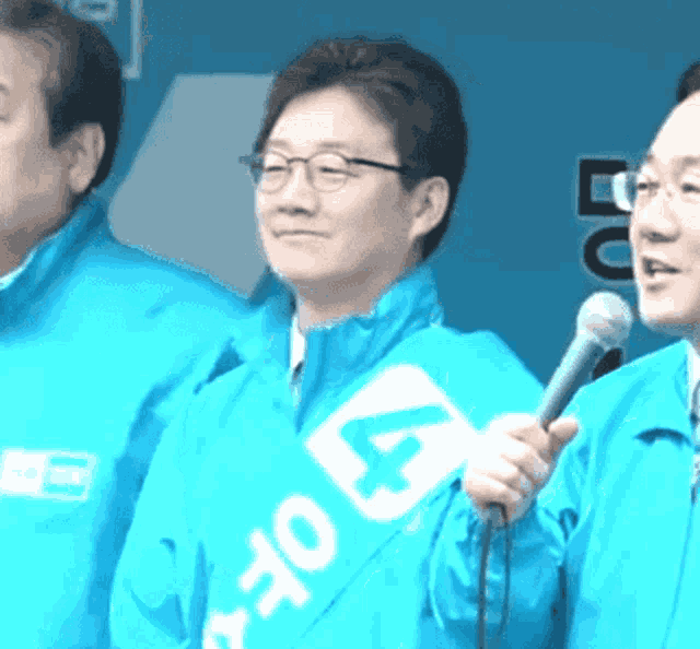 a man in a blue jacket holds a microphone while wearing a sash with the number 44 on it