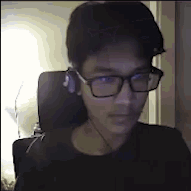 a young man wearing glasses and earbuds is sitting in a chair .