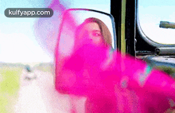 a woman is looking at herself in the rear view mirror of a vehicle .
