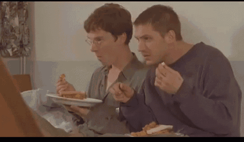 two men sitting at a table eating sandwiches and french fries