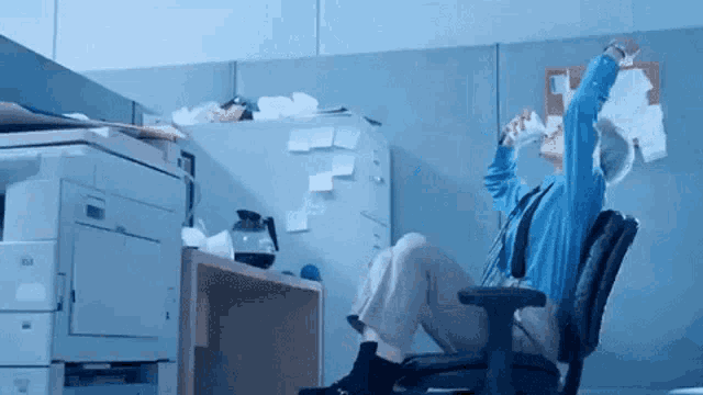 a man in a blue shirt is sitting in an office chair with his arms outstretched
