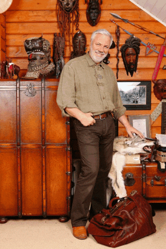 a man standing in front of a wooden wall with masks and a large brown bag