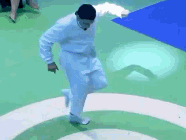 a man in a white shirt and white pants is dancing on a green floor .