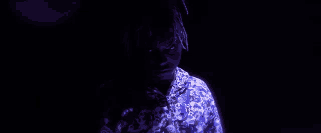 a man in a blue shirt is standing in the dark with a purple light behind him .