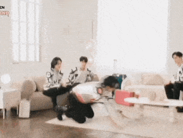 a group of people are sitting on a couch in a living room with a man kneeling on the floor .