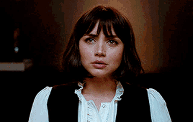 a woman with short hair and bangs is wearing a black vest and a white shirt