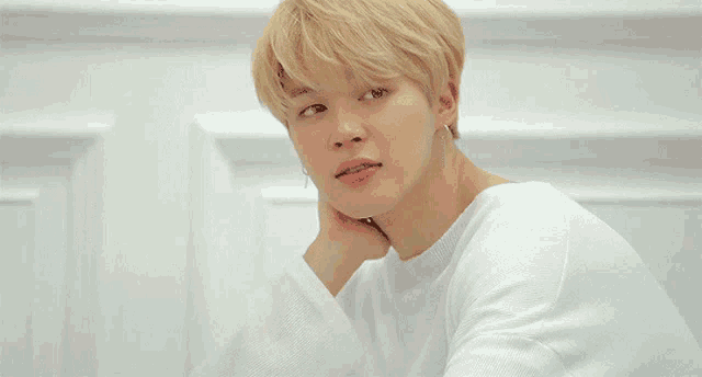 a young man with blonde hair is wearing a white sweater and earrings .