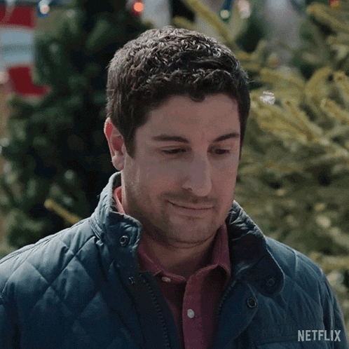 a man in a blue jacket is standing in front of a christmas tree and smiling .