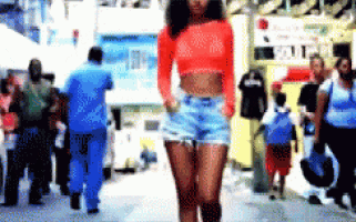 a woman in a red crop top and shorts is walking down the street