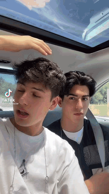 two young men are sitting in a car and one is touching the other 's hair .