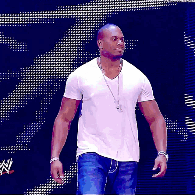 a man in a white shirt and blue jeans is walking on a stage with a wwe logo in the background