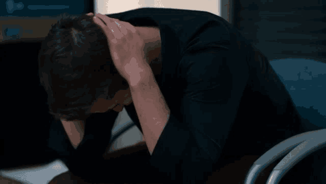 a man in a black shirt is sitting at a desk with his head in his hands