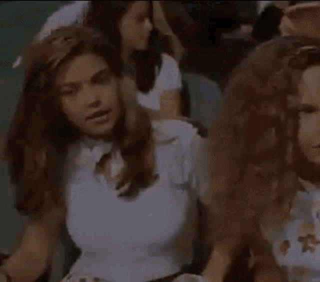 a woman in a white crop top is sitting in a crowd of people with her eyes closed .