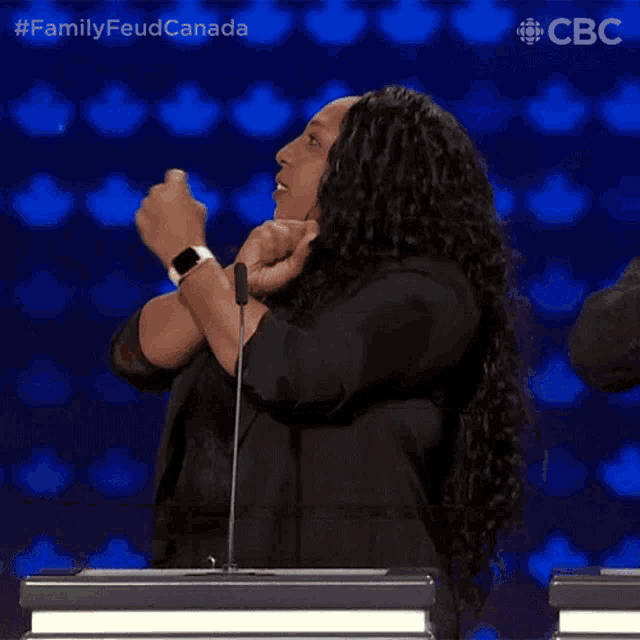 a woman giving a thumbs up in front of a microphone with the words family feud canada on the bottom