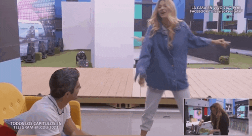 a woman in a denim jacket is dancing in front of a man in a yellow chair