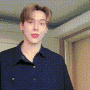 a young man in a blue shirt is standing in a room and making a funny face .