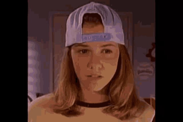 a young girl wearing a baseball cap and a yellow shirt is looking at the camera .