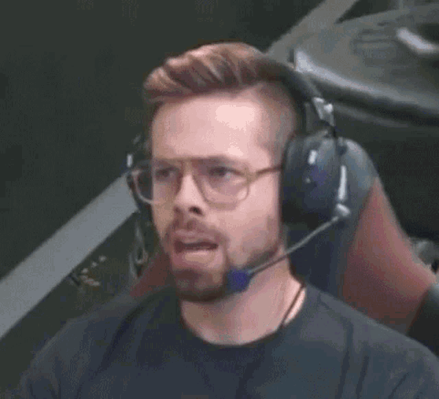 a man with a beard and glasses is wearing headphones and a microphone while sitting in a chair .