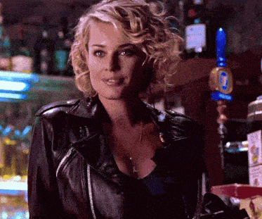 a blonde woman wearing a black leather jacket stands in front of a bar